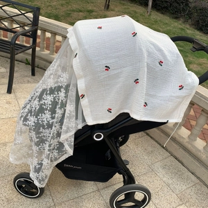 Detail of baby stroller net with red cherry pattern and white lace protective cover