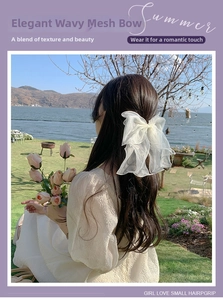 Detail of a large white tulle bow hair clip on long wavy hair with ethereal mesh streamers