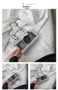 Detailed macro view of silver camera-shaped bag with pink feathers and ribbon