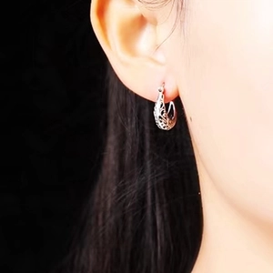 Detail showing elegant silver hollow patterned hoop earrings worn on a dark background
