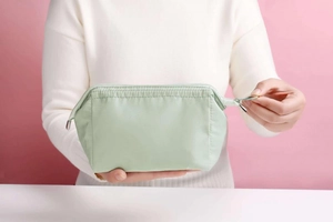 Waterproof mint green makeup bag made of nylon fabric held by hands on pink background