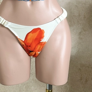 Detail of floral print bikini bottoms with elastic ruched side straps on cream fabric