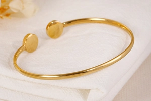Close-up of golden stainless steel open bangle with double flat disc charms and polished finish