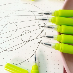 Macro view of green tulip pen with needle tip writing black ink on dot grid paper