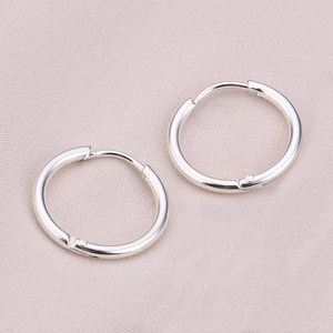 Close-up of classic polished silver steel hoop earrings on light pink fabric background