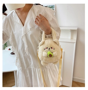 Detailed view of cat plush crossbody bag with avocado toy on a model in white dress