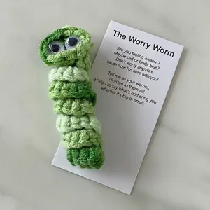 Handmade green crochet worry worm with googly eyes and poem card on marble background