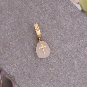 Détail de la boucle d'oreille en cristal rose avec croix dorée sur pierre grise