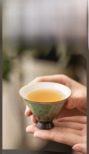 Close-up of hands holding a vintage kiln-fired ceramic teacup with green glaze and white interior