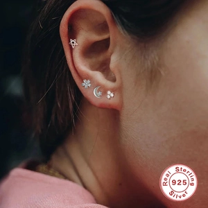 Close-up of multiple 925 sterling silver mini studs worn on ears showing various shapes