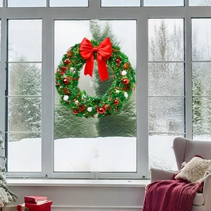 Close-up of a green Christmas wreath with red bows and pine cones on a window