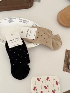 Détail de chaussettes basses à pois beiges et noires présentées sur une assiette décorative