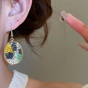 Close-up of golden oval earrings with colorful rhinestones on a female model