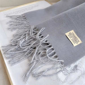 Close-up of grey soft scarf with elegant tassels and stitched brand label detail