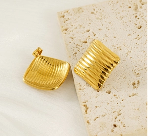 Detailed view of square gold earrings with vertical corrugated texture and glossy finish