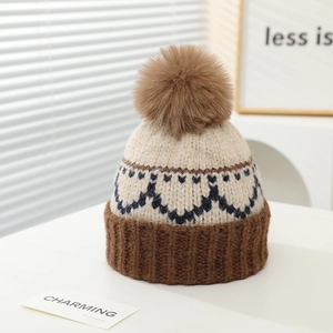 Detail einer Strickmütze mit braunem Pompon, Herzmustern und umgeschlagenem Rand