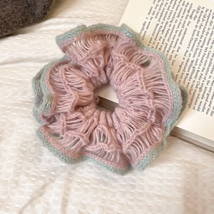 Detail of pink and cyan knitted flower scrunchie on a soft quilted surface