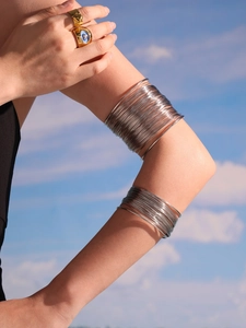Detail of multi-layer silver wire arm cuff and gold ring with blue enamel against blue sky