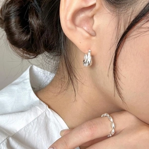 Close-up of minimalist sterling silver irregular earrings and beaded ring on model