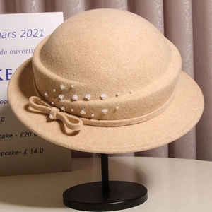 Detail of beige wool felt cloche hat with elegant bow and pearl floral embellishments