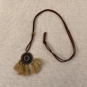 Details einer langen Boho-Halskette mit Bronzemedaillon und khakifarbenen Quasten