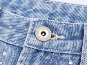 Vue macro du bouton en métal argenté et détails en strass sur tissu denim bleu clair