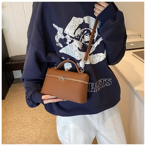 Brown litchi grain leather box handbag with top handle and zip closure held by a model