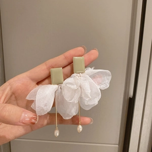 Detail of sage green floral mesh earrings with pearls held by a hand on a clean background