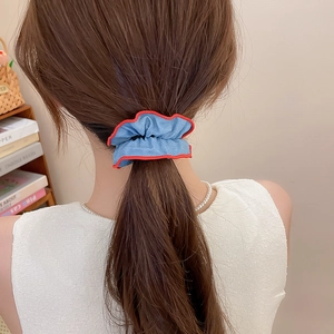 Blue ruffled fabric hair tie with red wavy edges shown on a low ponytail hairstyle