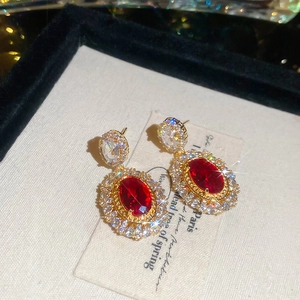 Detail of vintage style gold plated oval red gem earrings with white crystal halo