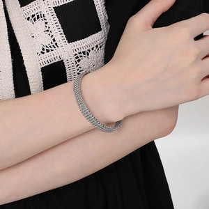 Detail of silver C-shaped braided steel mesh bracelet on wrist with textured metal weave