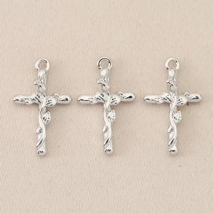 Close-up of three silver baroque cross pendants with intricate vine relief patterns