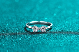 Macro view of bow ring with two heart-shaped moissanite stones on green glitter background