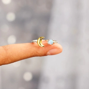 Detail of s925 silver moon ring with gold crescent and glowing opal stone on finger