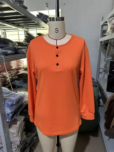 Detail of orange waffle knit Henley top featuring three black buttons and round neck texture
