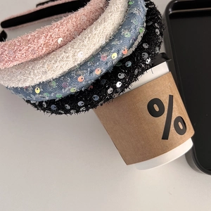Detail of four sequined velvet headbands in pink white blue and black on a coffee cup