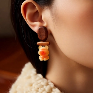 Detail of a cute wooden bear pendant earring worn by a model against a warm knit background