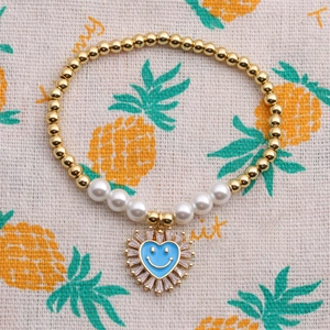 Dettaglio del bracciale con perle e cuore placcato oro con ciondolo occhio blu su stoffa