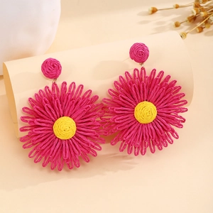 Detail of handmade raffia sunflower earrings in fuchsia and yellow with woven texture