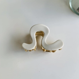 Close-up of a wavy white hair claw clip with a golden metal spring on a white backdrop