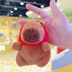 Close-up of a plush Capybara keychain wearing a tiny red hooded cape with silver chain