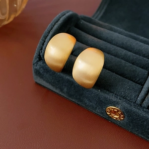 Detailed close-up of matte gold geometric C-shaped earrings inside a blue velvet box