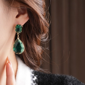 Dettaglio degli orecchini pendenti con cristalli verde smeraldo indossati dalla modella