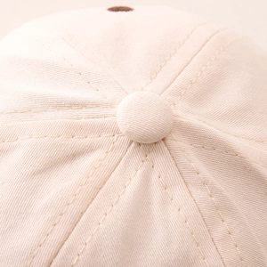 Macro view of beige cotton twill baseball cap showing top button and hexagonal stitching