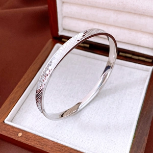Detailed close-up of a silver metal bangle with honeycomb textured engraving on a jewelry box