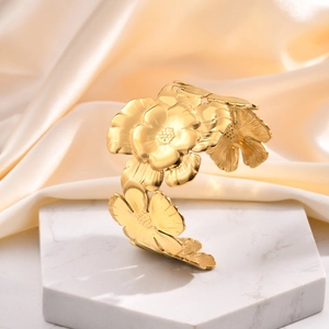 Golden flower petal cuff bracelet displayed on marble base with beige silk background