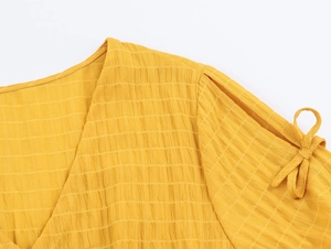 Dettaglio dell'abito giallo con scollo a V, tessuto stropicciato e manica con fiocco