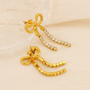 Detail of elegant gold bow earrings with dangling crystal tassels on a soft fabric base