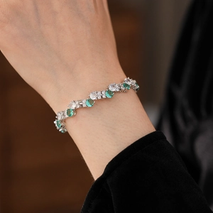 Detailed close-up of a silver bracelet with alternating green zircons and white crystals