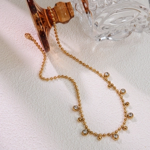 Detail of gold beaded necklace with transparent zircon pendants on a white background